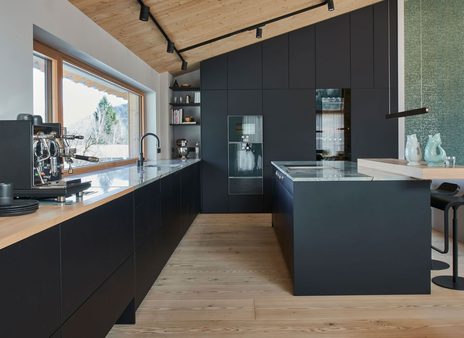 Küche mit besonders gemustertem Naturstein und schwarzen Mattlackfronten bis unters Dach.