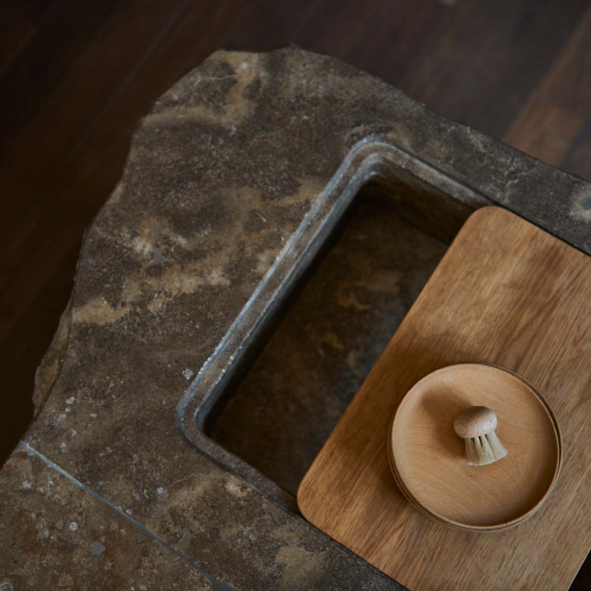 Blick in ein in Stein gefrästes Spülbecken mit individuell gefertigtem Holzbrett.